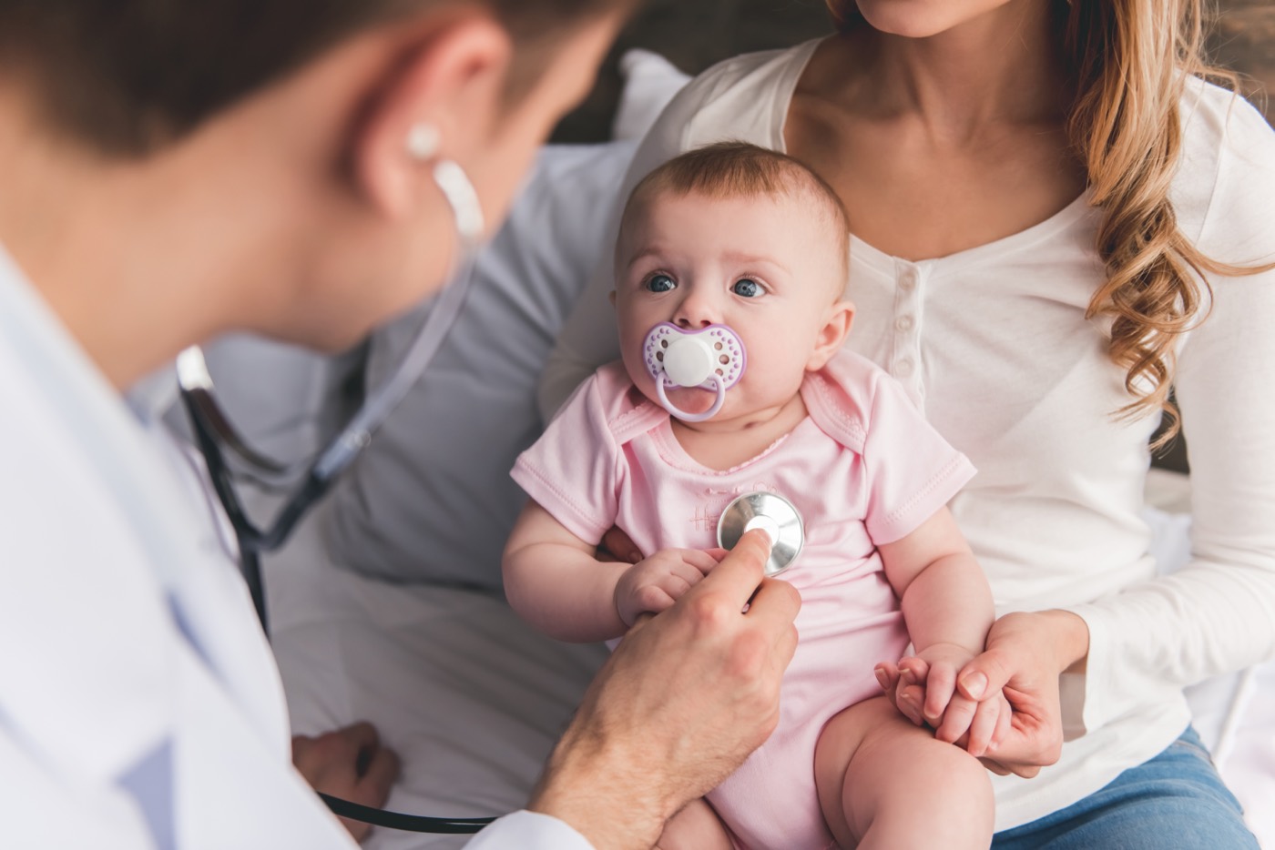 A doctor examining an infant held by their mother