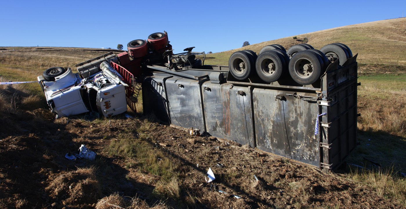 Overturned semi-truck and trailer in a roadside field